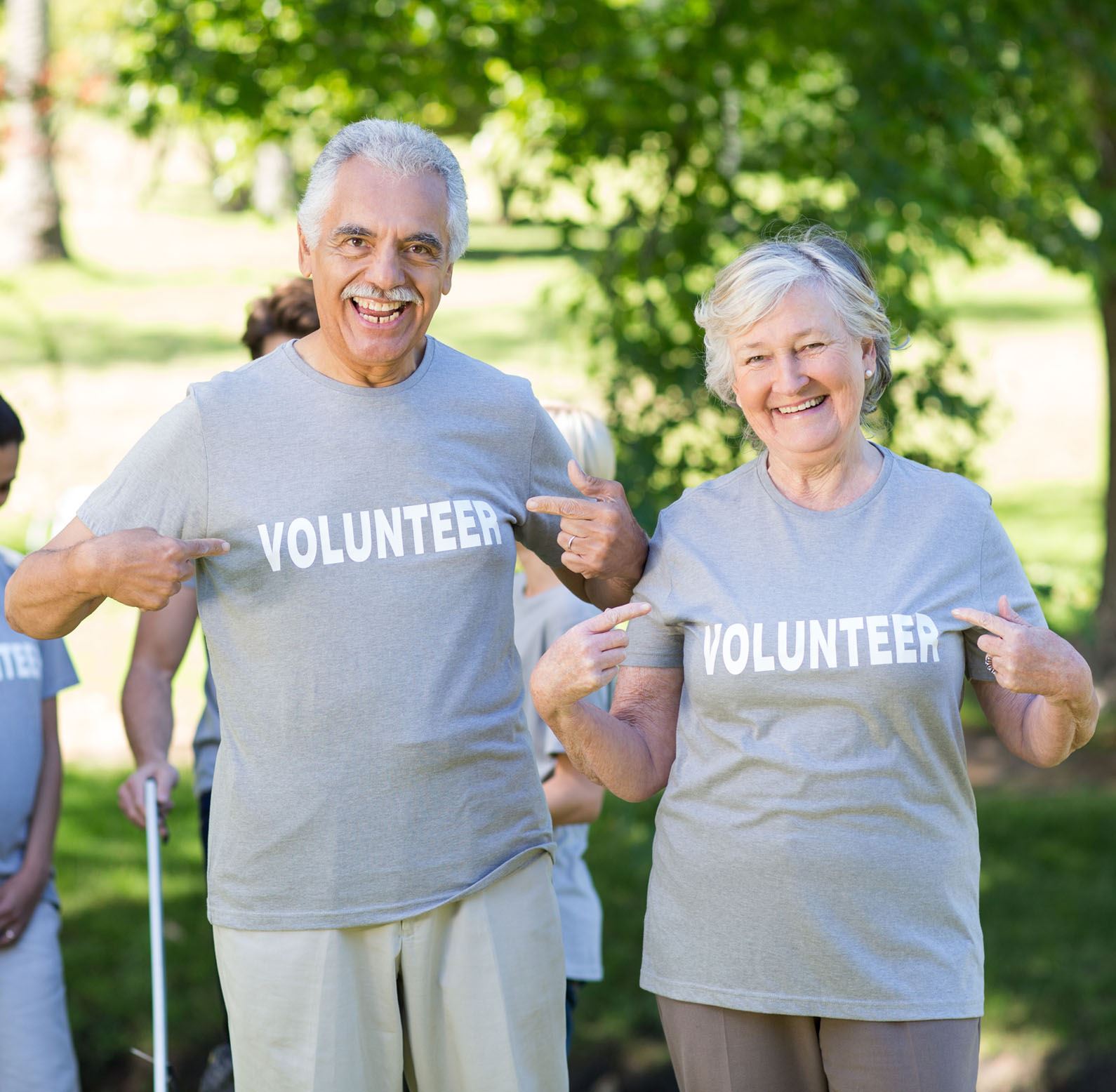 Older man and older woman happily pointing to their gray Volunteer shirt while outside